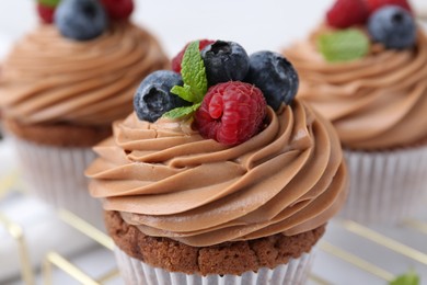 Photo of Tasty cupcakes with chocolate cream and berries on table, closeup