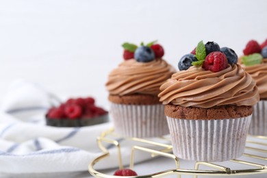 Photo of Tasty cupcakes with chocolate cream and berries on table, closeup