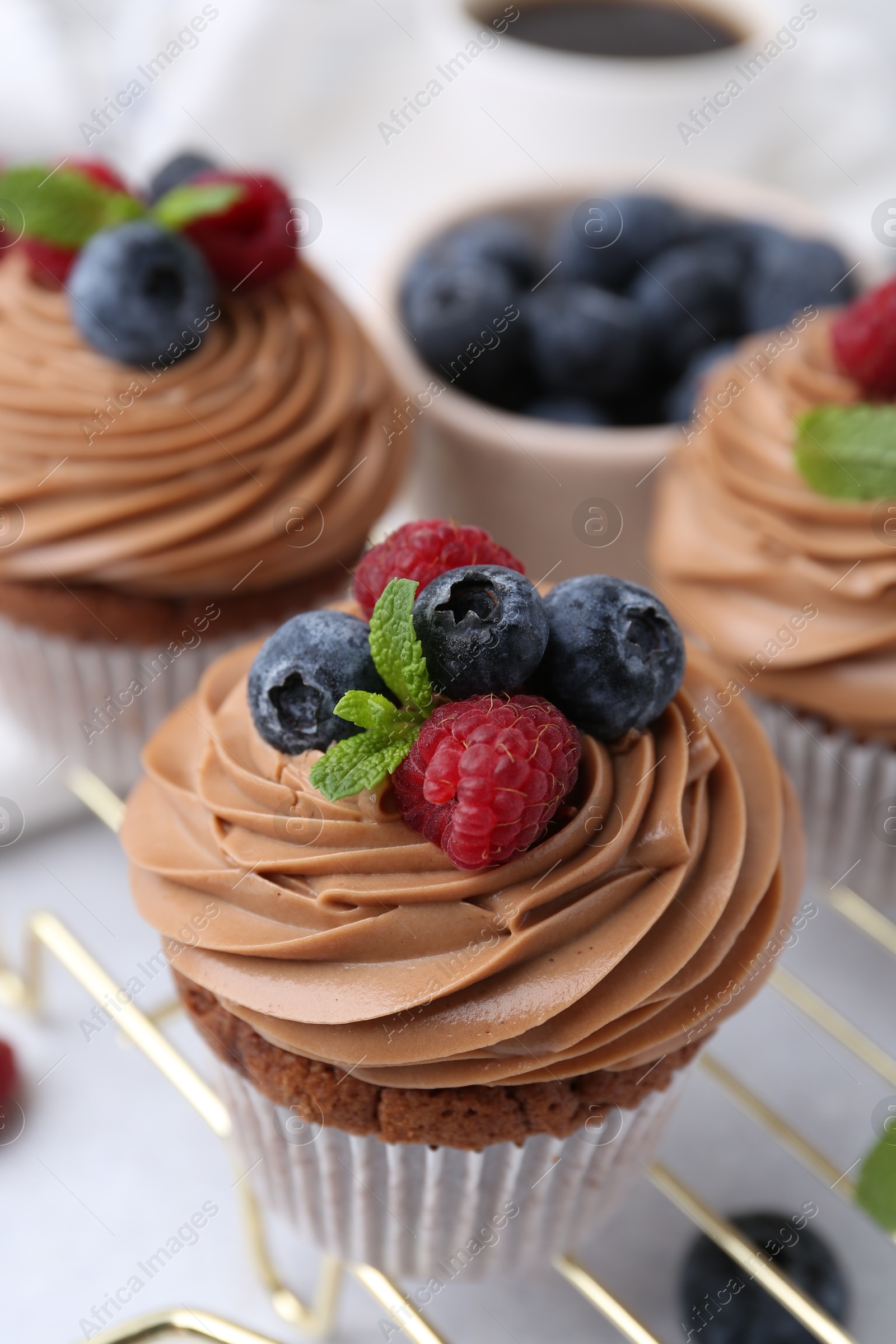 Photo of Tasty cupcakes with chocolate cream and berries on white table, closeup