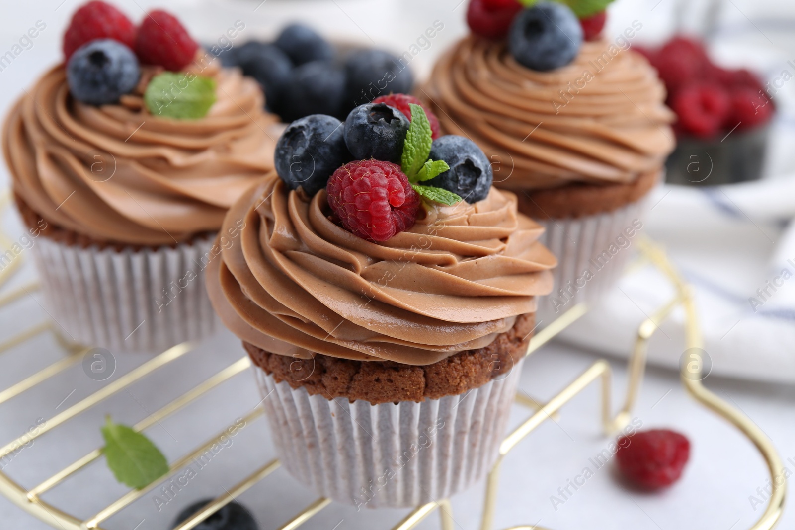 Photo of Tasty cupcakes with chocolate cream and berries on white table, closeup