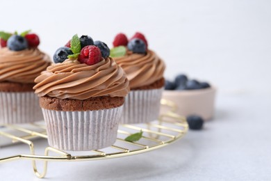 Photo of Tasty cupcakes with chocolate cream and berries on white table, closeup. Space for text