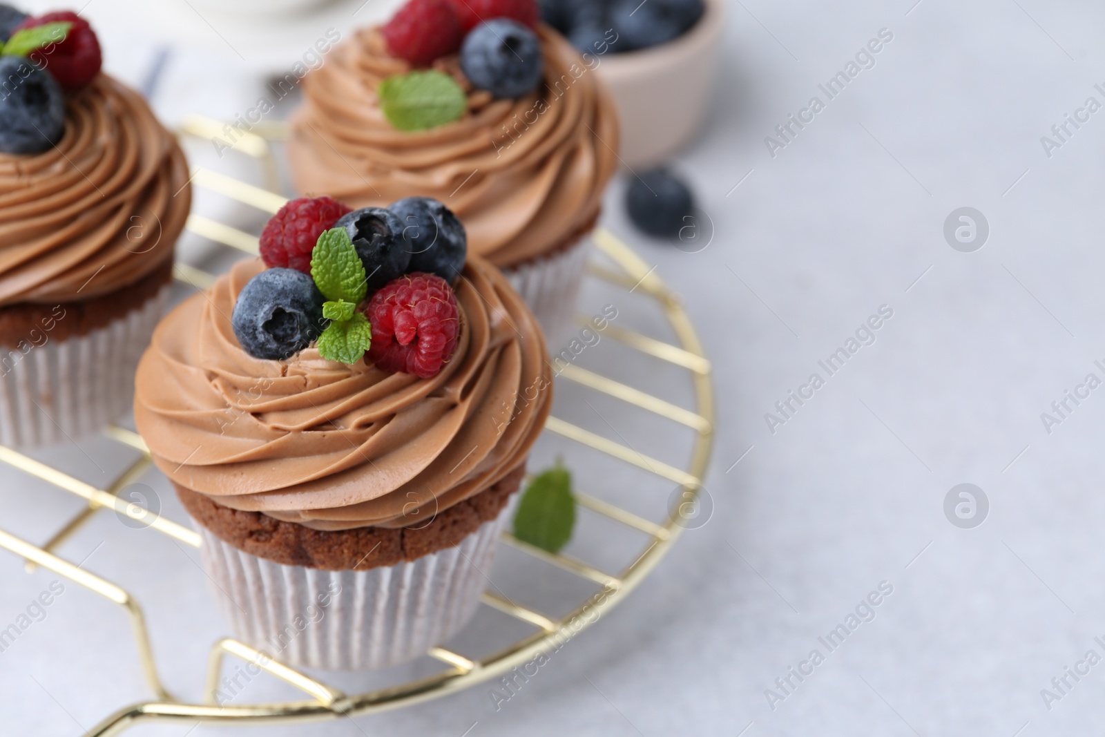 Photo of Tasty cupcakes with chocolate cream and berries on white table, closeup. Space for text