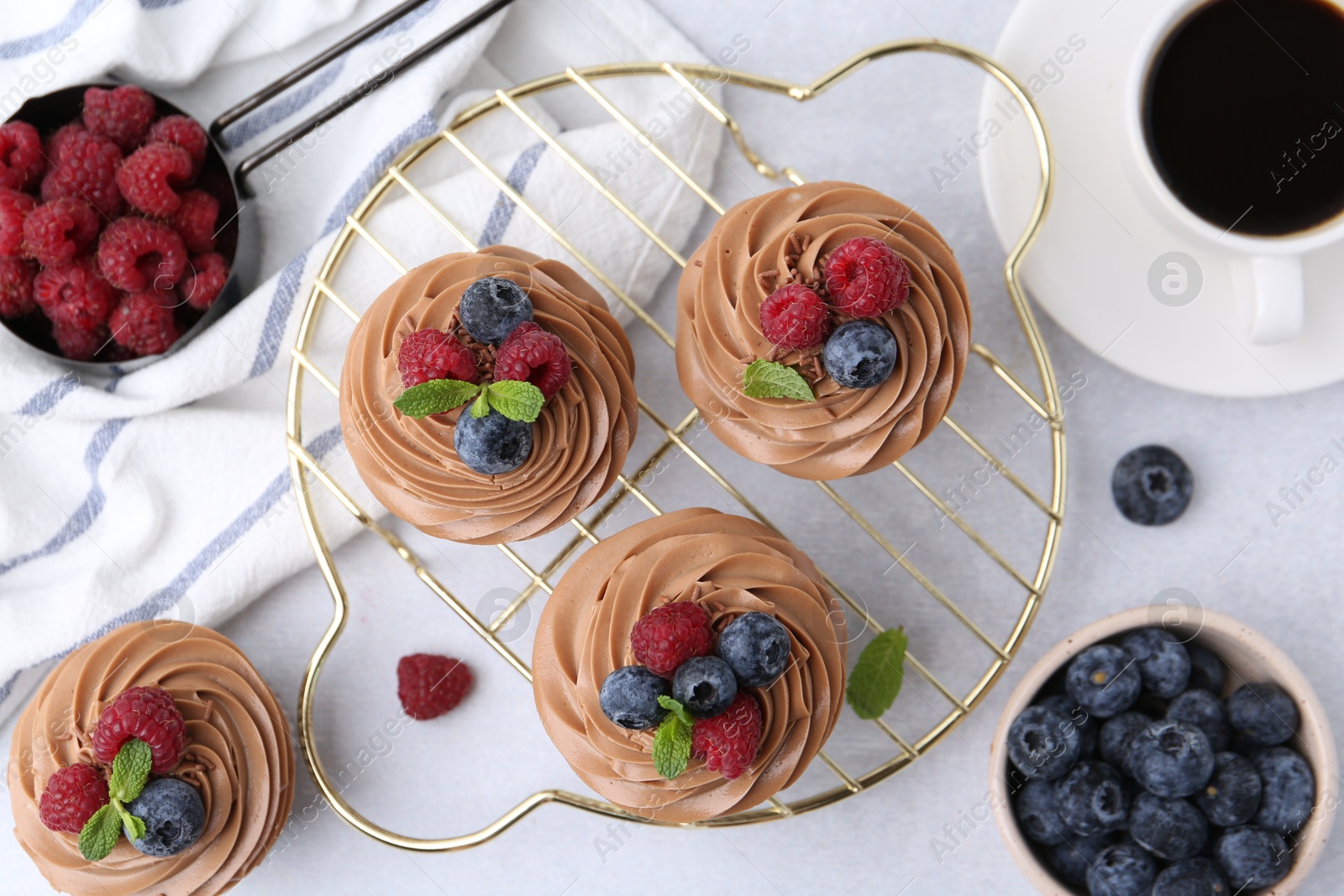 Photo of Tasty cupcakes with chocolate cream and berries on white table, flat lay