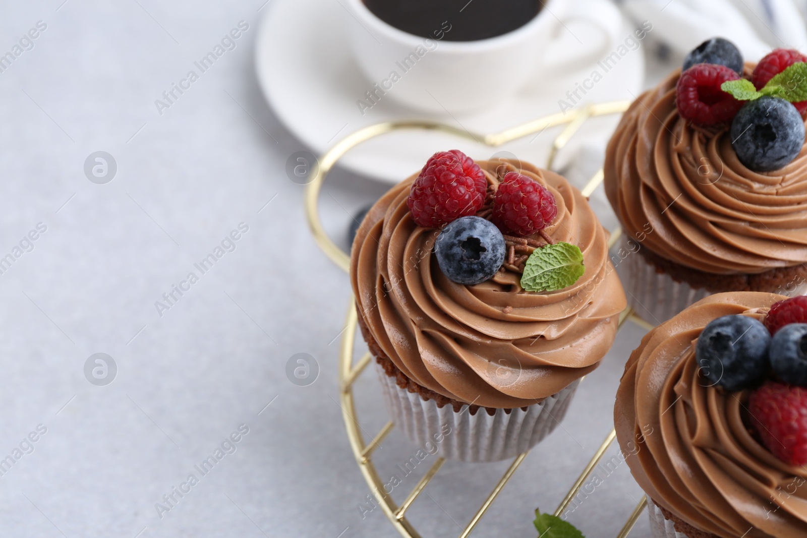 Photo of Tasty cupcakes with chocolate cream and berries on white table, closeup. Space for text