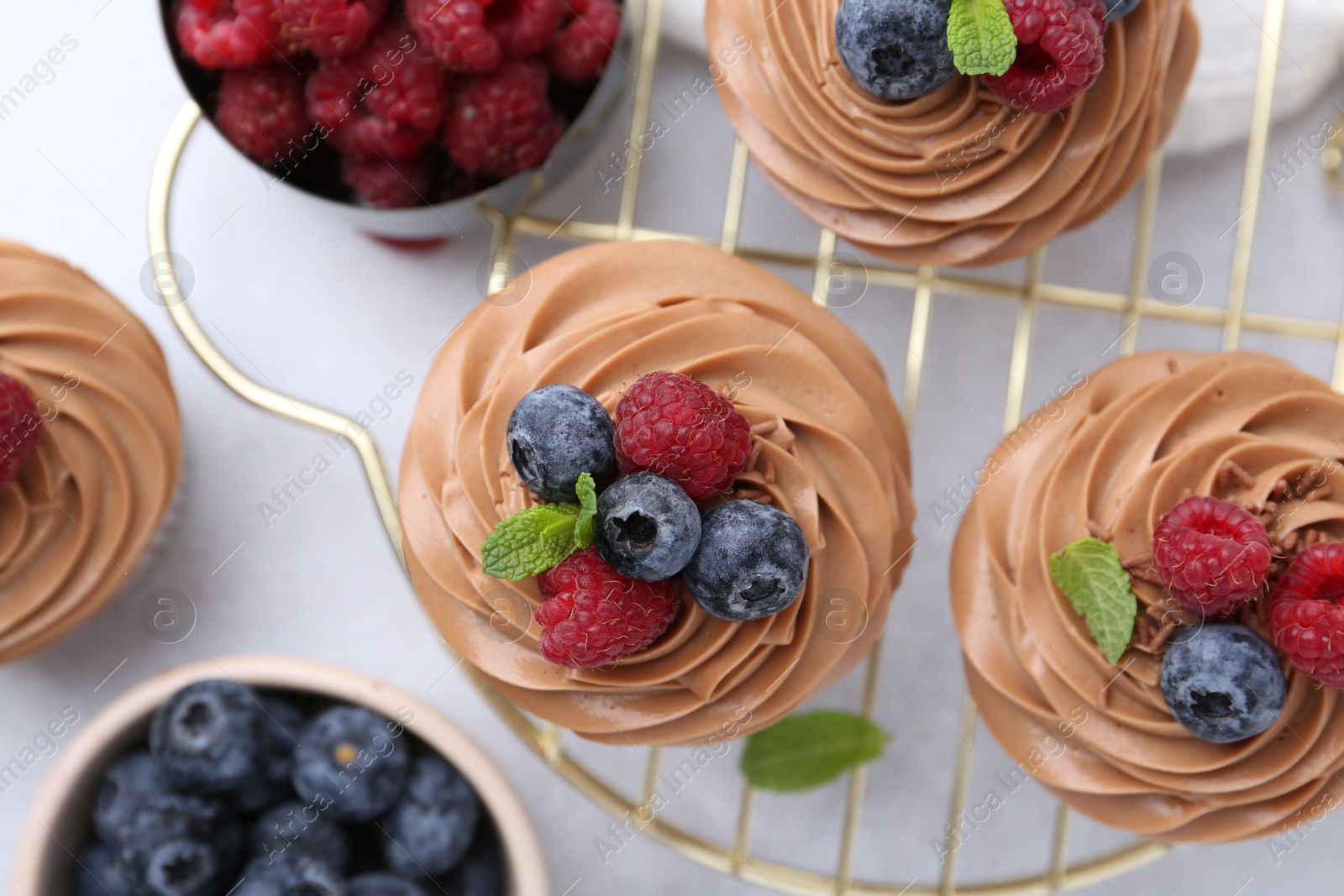 Photo of Tasty cupcakes with chocolate cream and berries on white table, flat lay