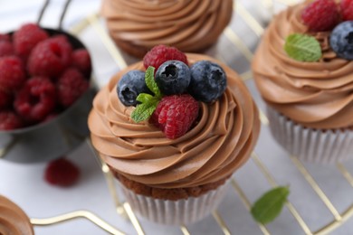 Photo of Tasty cupcakes with chocolate cream and berries on white table, closeup