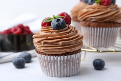 Photo of Tasty cupcakes with chocolate cream and berries on white table, closeup