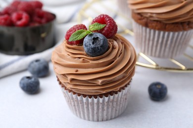 Photo of Tasty cupcakes with chocolate cream and berries on white table, closeup