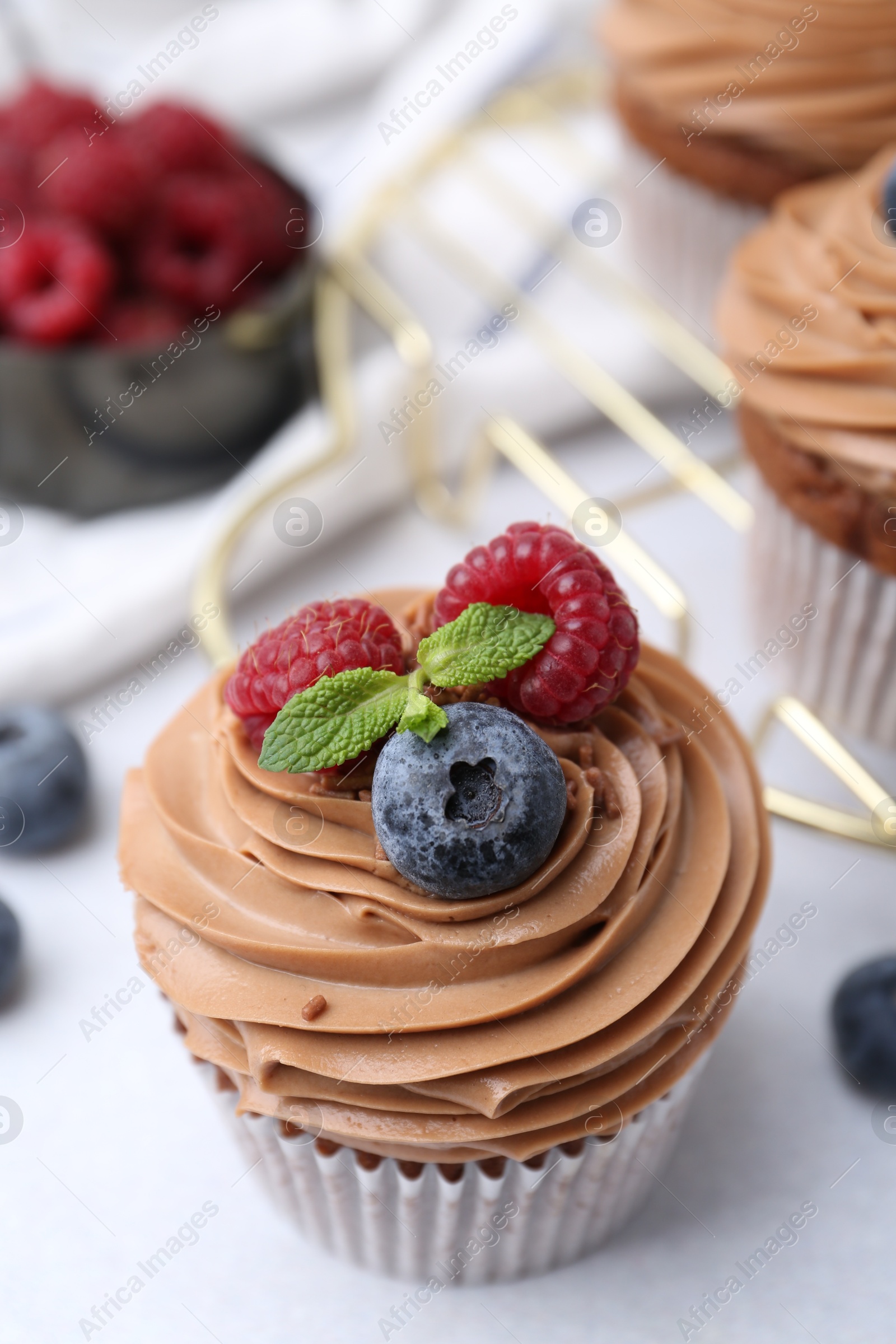 Photo of Tasty cupcakes with chocolate cream and berries on white table, closeup