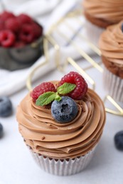 Photo of Tasty cupcakes with chocolate cream and berries on white table, closeup