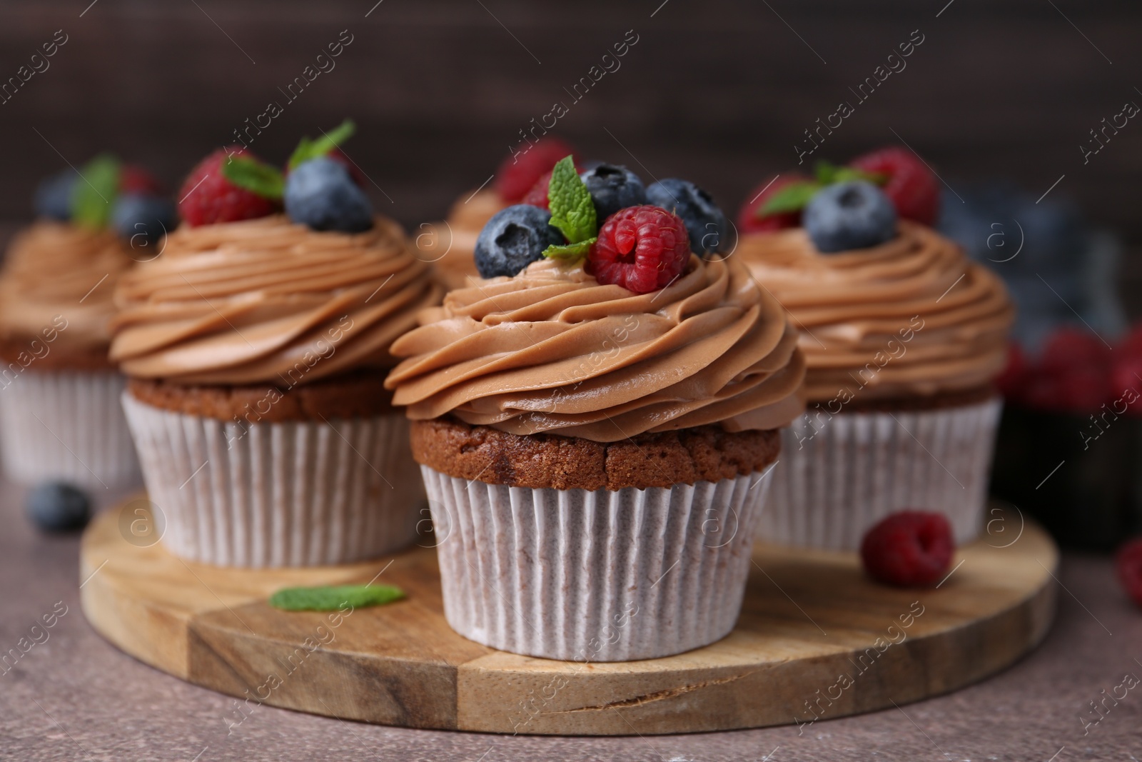 Photo of Tasty cupcakes with chocolate cream and berries on brown table, closeup