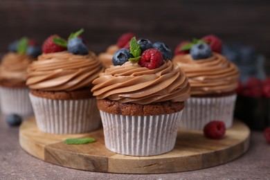 Photo of Tasty cupcakes with chocolate cream and berries on brown table, closeup