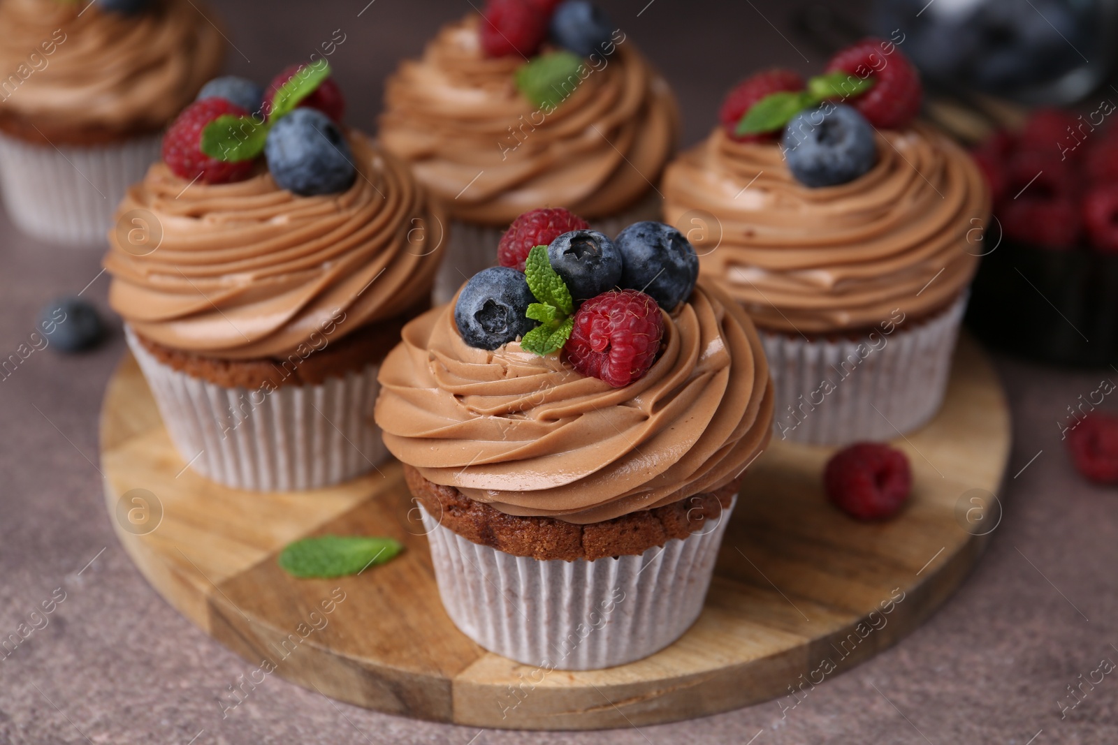 Photo of Tasty cupcakes with chocolate cream and berries on brown table, closeup