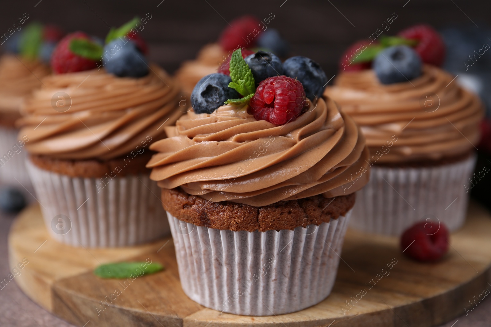 Photo of Tasty cupcakes with chocolate cream and berries on brown table, closeup