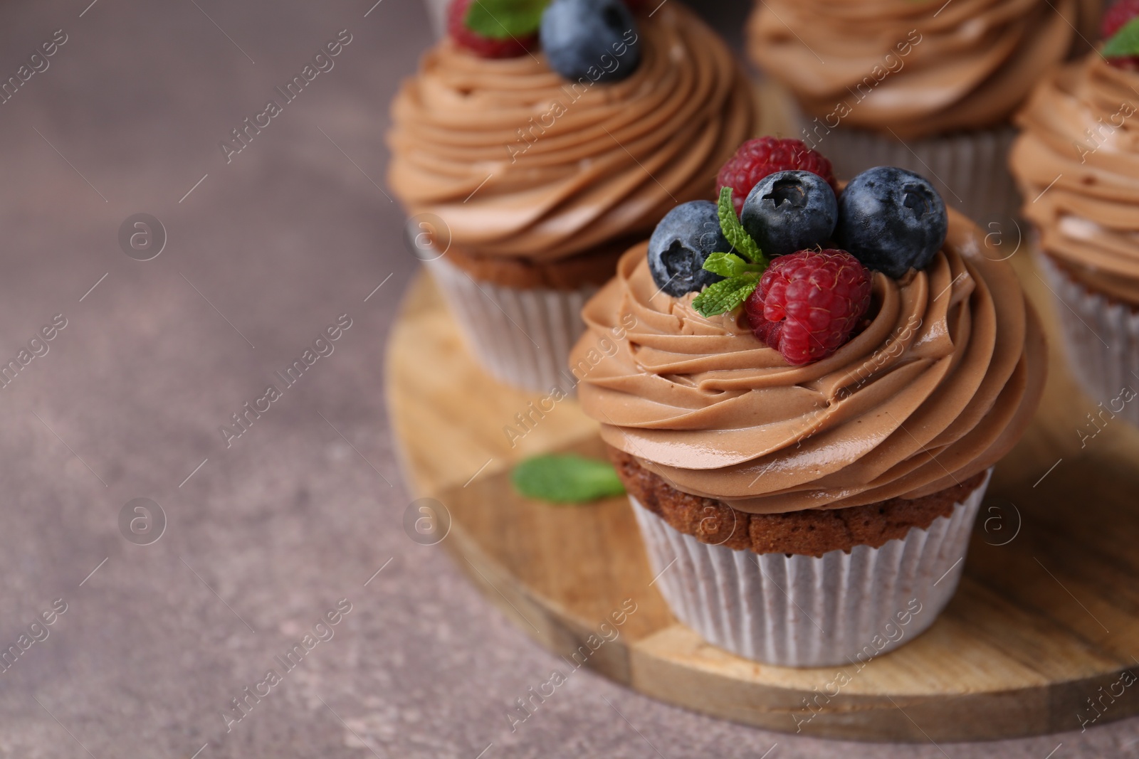 Photo of Tasty cupcakes with chocolate cream and berries on brown table, closeup. Space for text