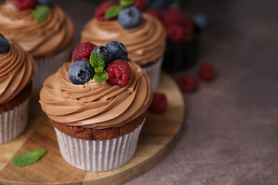 Photo of Tasty cupcakes with chocolate cream and berries on brown table, closeup. Space for text