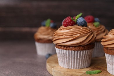 Photo of Tasty cupcakes with chocolate cream and berries on brown table, closeup. Space for text