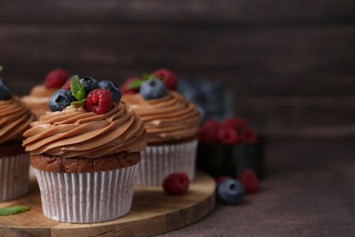 Photo of Tasty cupcakes with chocolate cream and berries on brown table, closeup. Space for text