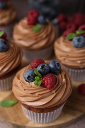 Photo of Tasty cupcakes with chocolate cream and berries on brown table, closeup