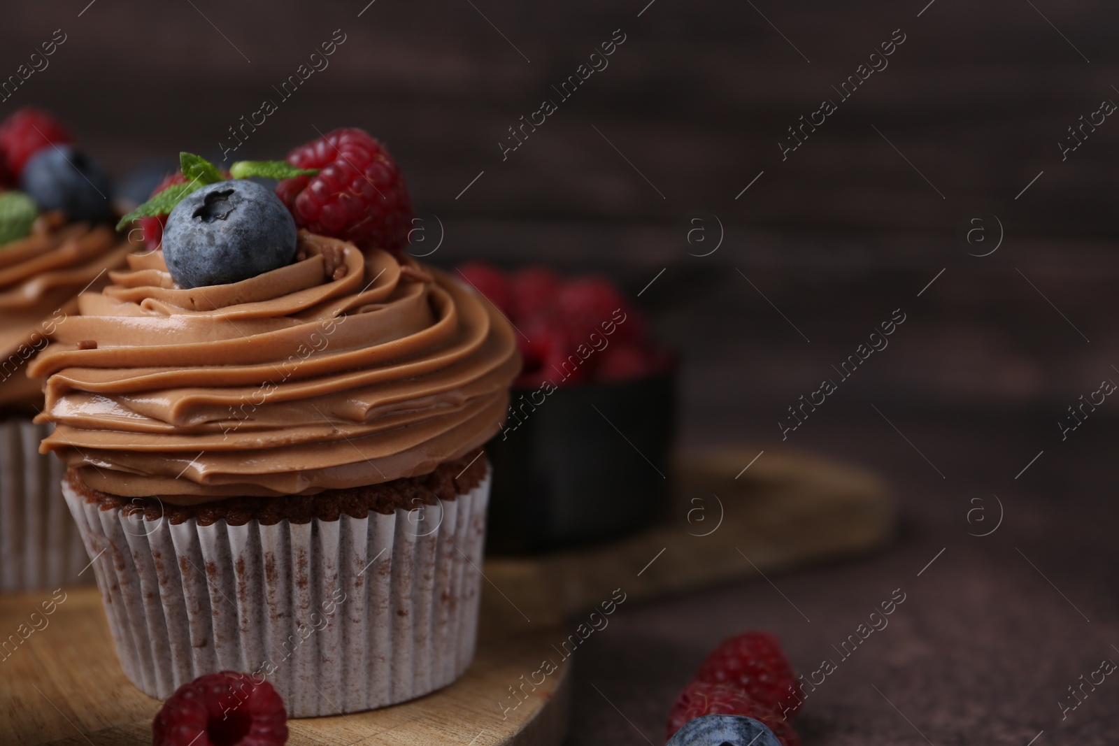 Photo of Tasty cupcakes with chocolate cream and berries on brown table, closeup. Space for text