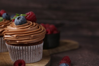 Photo of Tasty cupcakes with chocolate cream and berries on brown table, closeup. Space for text