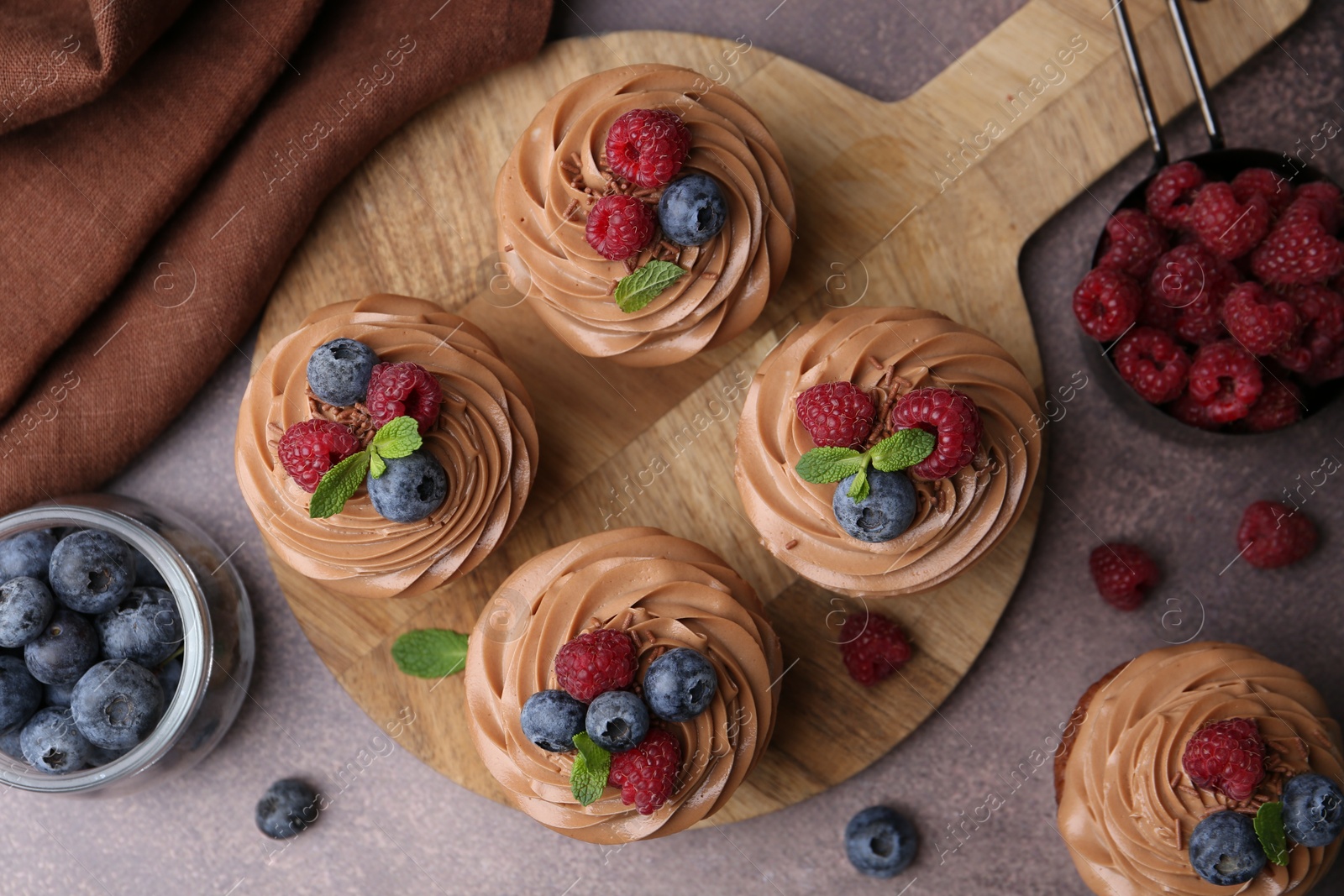 Photo of Tasty cupcakes with chocolate cream and berries on brown table, flat lay