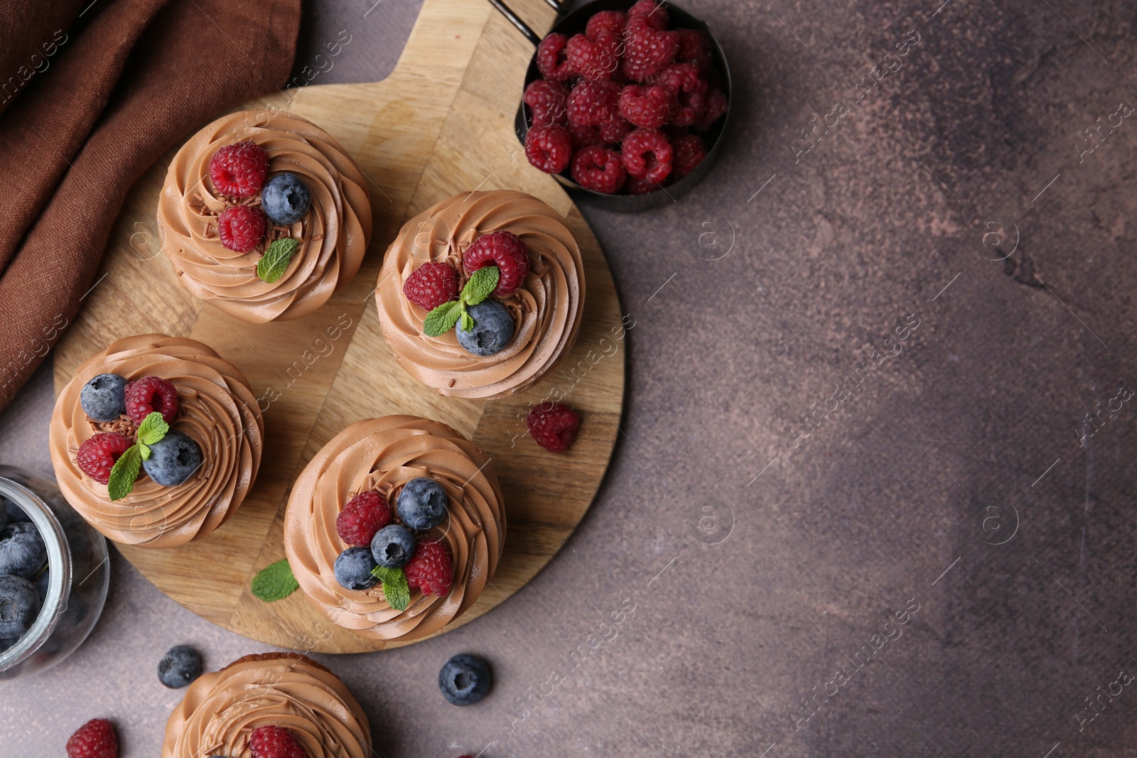 Photo of Tasty cupcakes with chocolate cream and berries on brown table, flat lay. Space for text