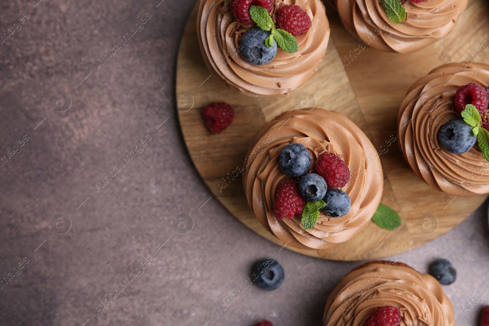 Photo of Tasty cupcakes with chocolate cream and berries on brown table, flat lay. Space for text