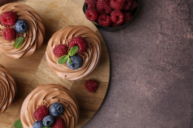 Photo of Tasty cupcakes with chocolate cream and berries on brown table, flat lay. Space for text