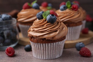 Photo of Tasty cupcakes with chocolate cream and berries on brown table, closeup