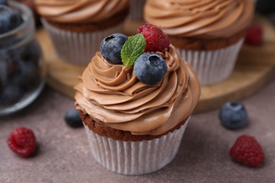 Photo of Tasty cupcakes with chocolate cream and berries on brown table, closeup