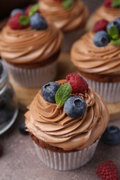 Photo of Tasty cupcakes with chocolate cream and berries on brown table, closeup