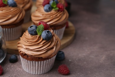 Photo of Tasty cupcakes with chocolate cream and berries on brown table, closeup. Space for text