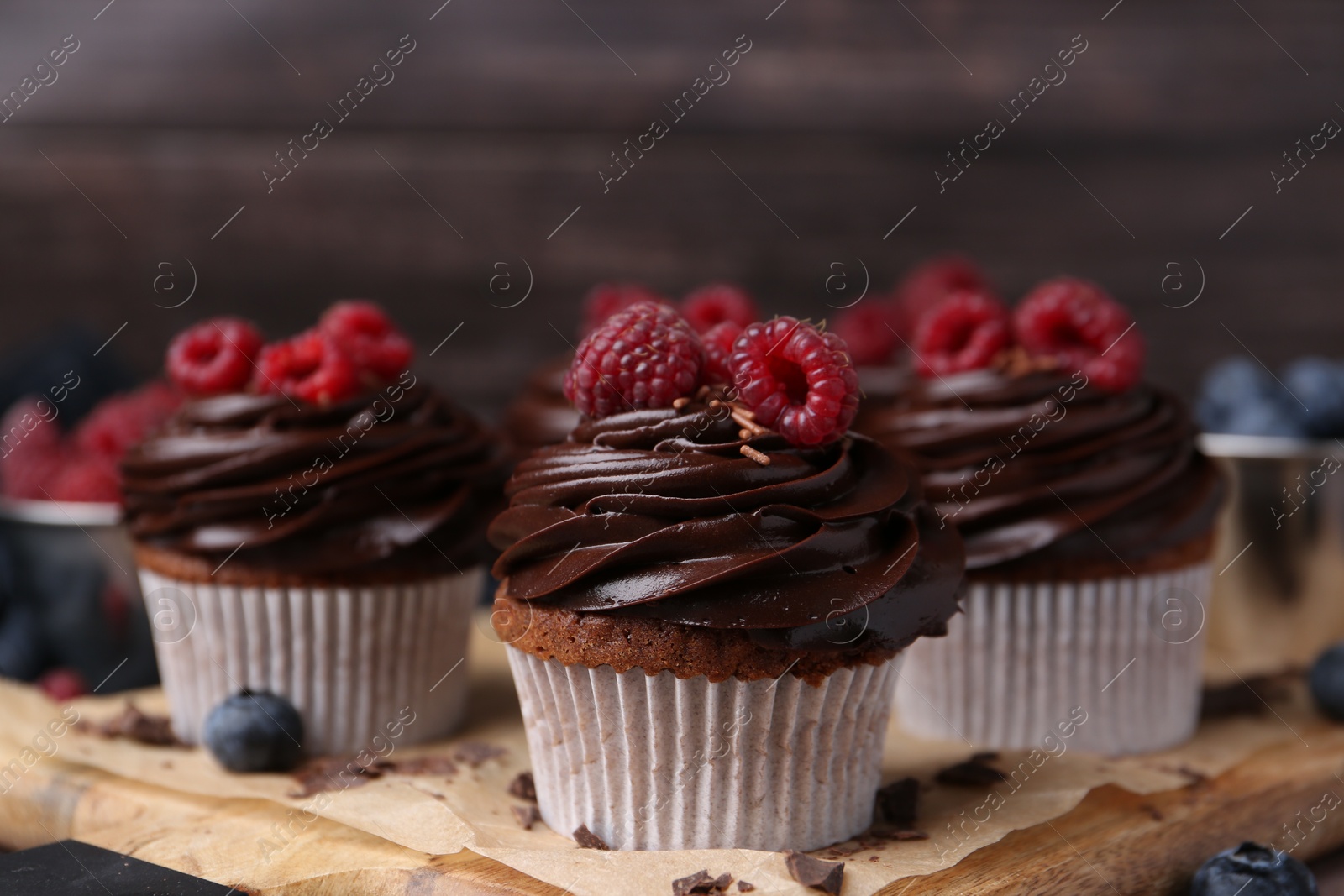 Photo of Tasty cupcakes with chocolate cream and raspberries on wooden board, closeup