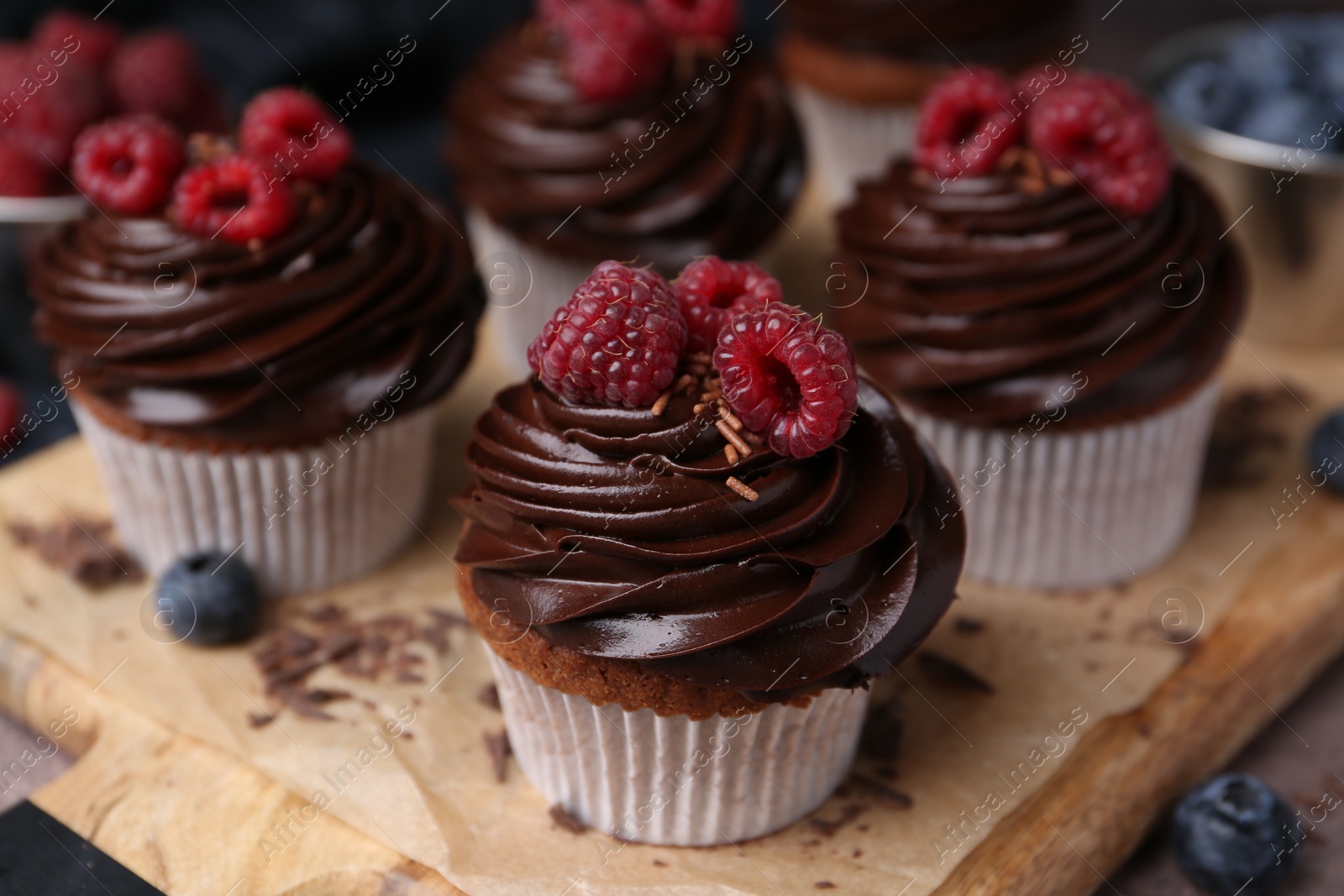 Photo of Tasty cupcakes with chocolate cream and berries on brown table, closeup