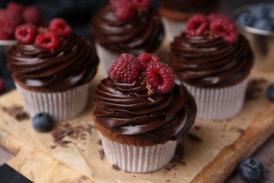 Photo of Tasty cupcakes with chocolate cream and berries on brown table, closeup