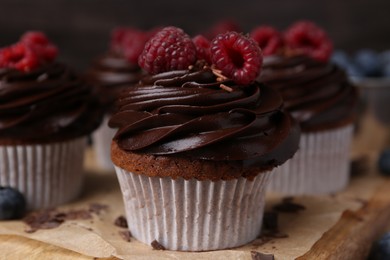 Photo of Tasty cupcakes with chocolate cream and raspberries on wooden board, closeup