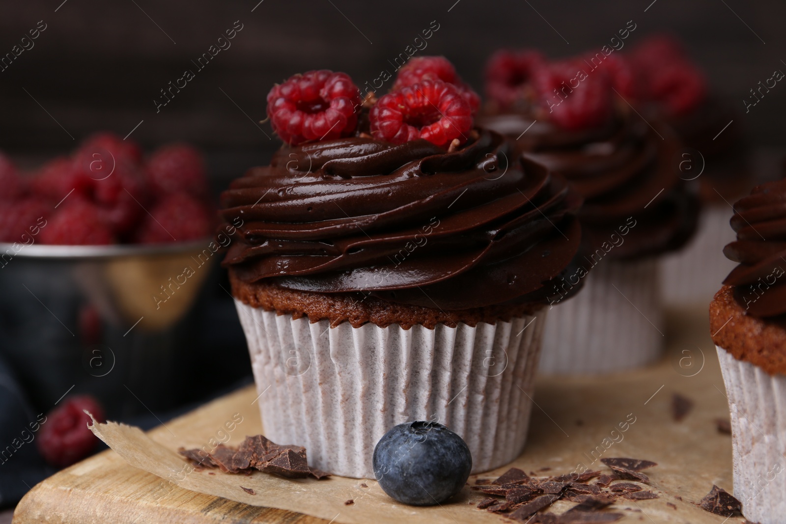 Photo of Tasty cupcakes with chocolate cream and raspberries on wooden board, closeup