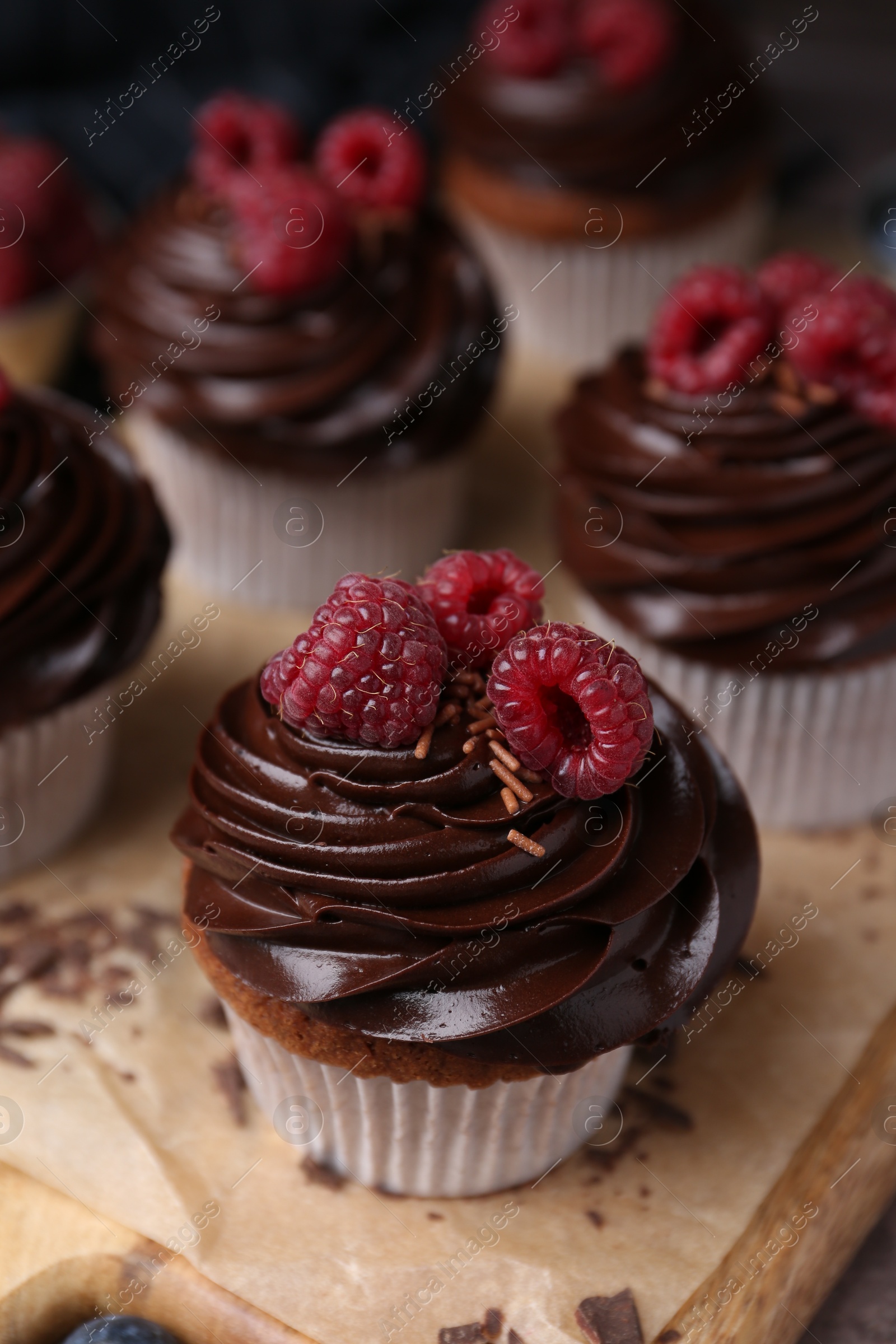 Photo of Tasty cupcakes with chocolate cream and raspberries on wooden board, closeup