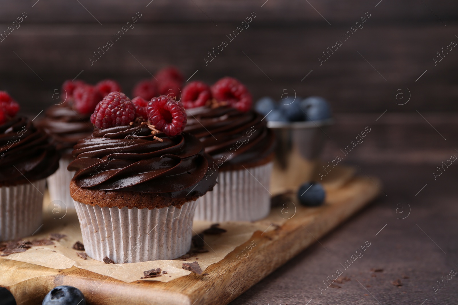 Photo of Tasty cupcakes with chocolate cream and raspberries on brown table, closeup