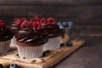 Photo of Tasty cupcakes with chocolate cream and raspberries on brown table, closeup