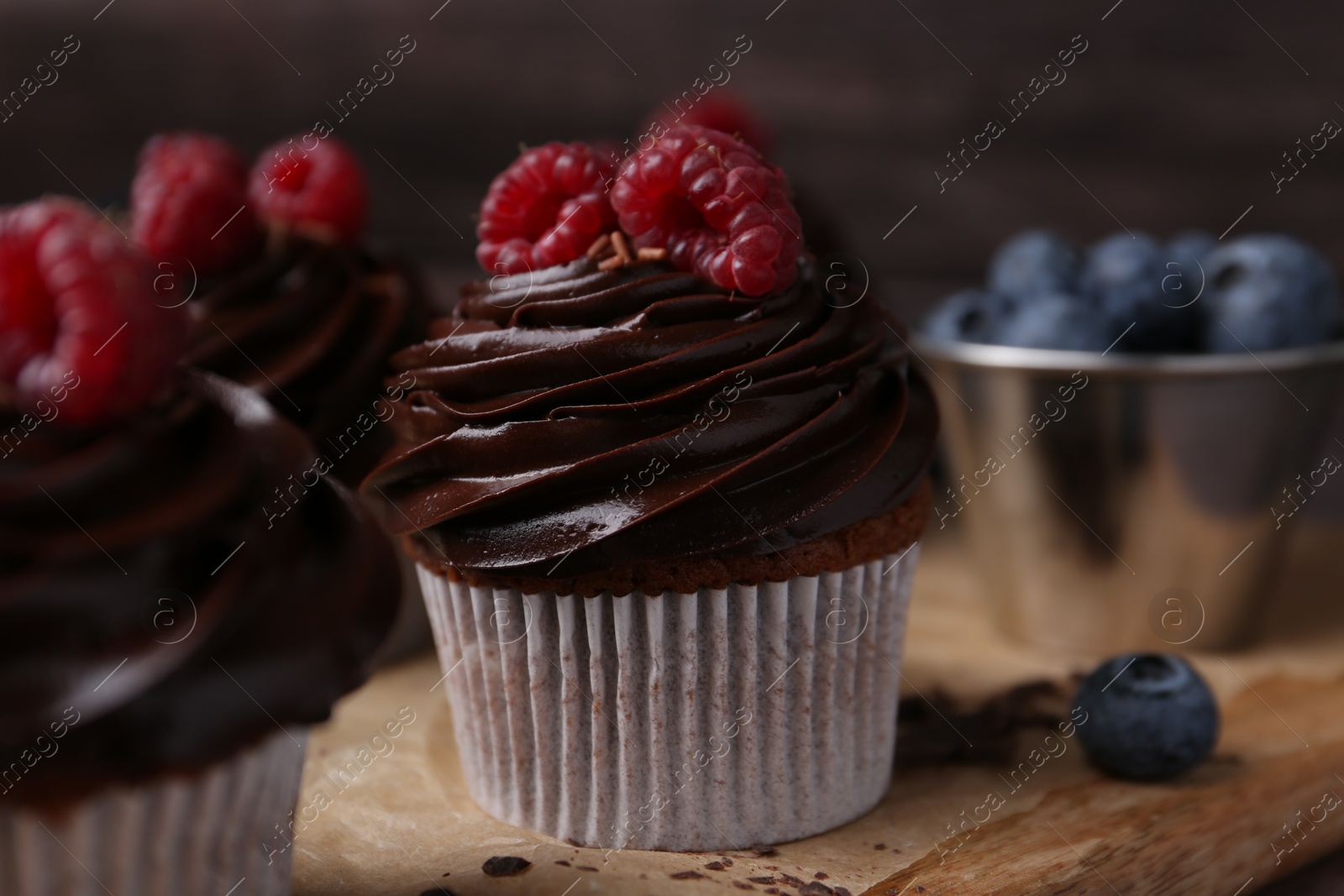 Photo of Tasty cupcakes with chocolate cream and berries on wooden board, closeup