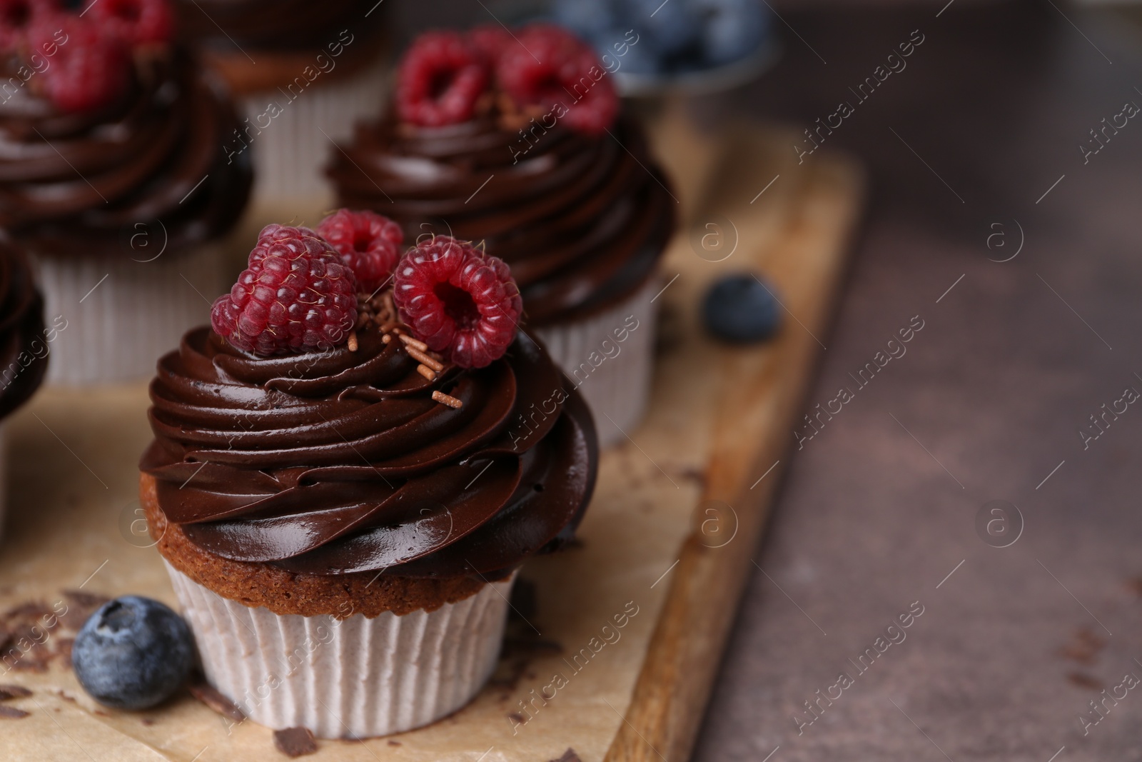 Photo of Tasty cupcakes with chocolate cream and berries on brown table, closeup. Space for text