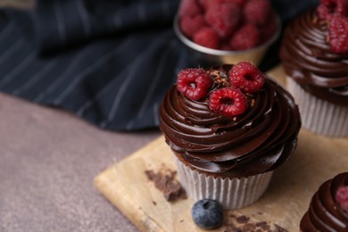 Photo of Tasty cupcakes with chocolate cream and berries on brown table, closeup. Space for text