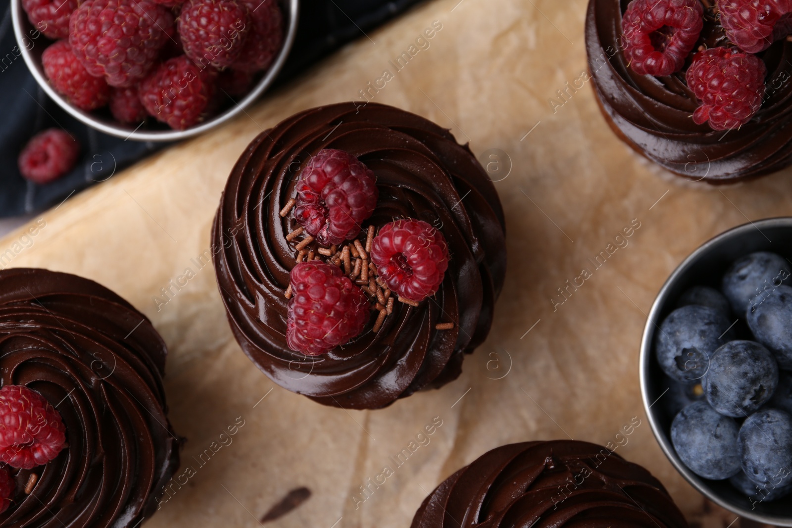 Photo of Tasty cupcakes with chocolate cream and raspberries on wooden board, flat lay