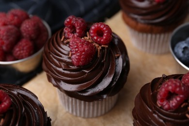 Photo of Tasty cupcakes with chocolate cream and berries on wooden board, closeup