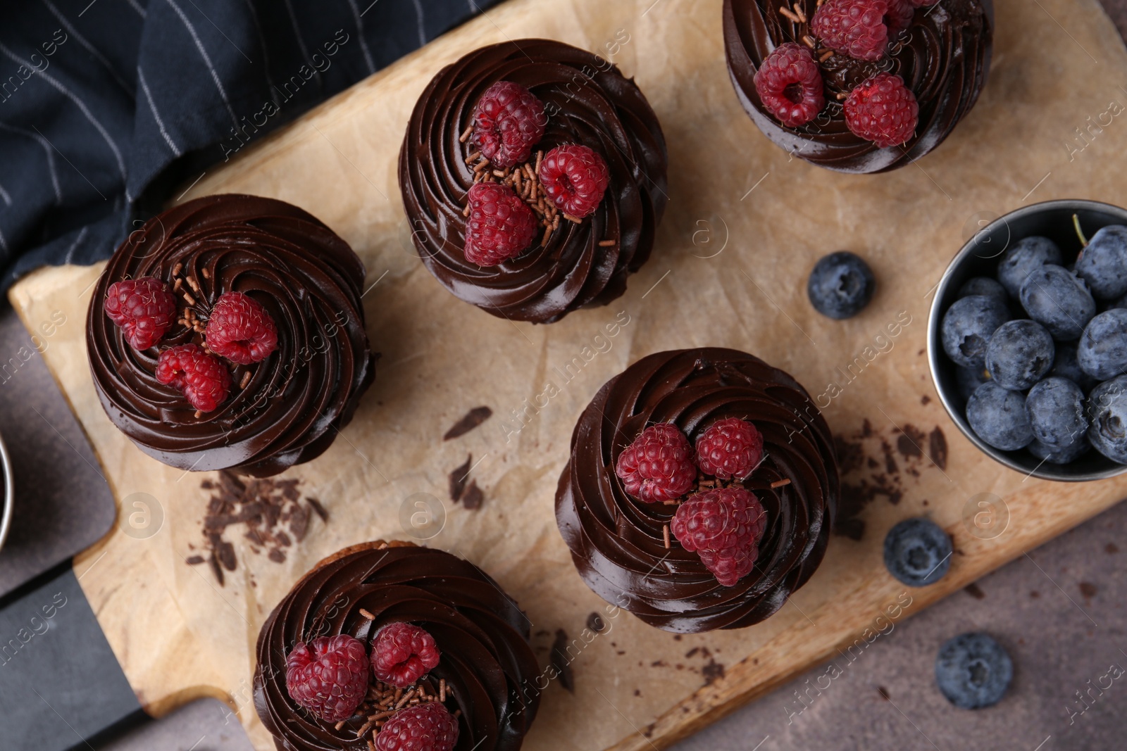 Photo of Tasty cupcakes with chocolate cream and berries on brown table, flat lay