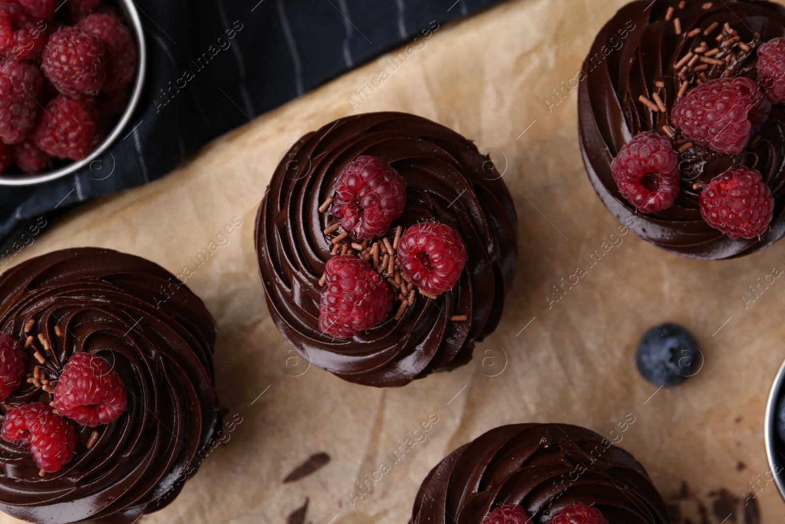 Photo of Tasty cupcakes with chocolate cream and raspberries on wooden board, flat lay