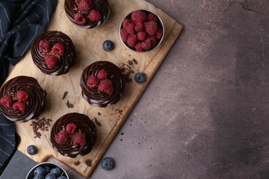 Photo of Tasty cupcakes with chocolate cream and berries on brown table, flat lay. Space for text