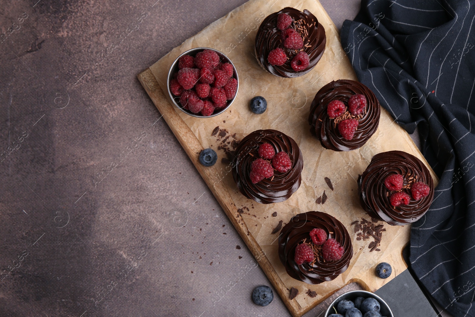 Photo of Tasty cupcakes with chocolate cream and berries on brown table, flat lay. Space for text